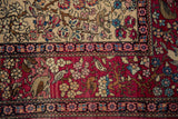 The pictorial border of an antique Isfahan rug showing a forest scene with birds against a cochineal red ground.
