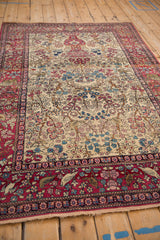Angled view of an antique Isfahan rug's ivory field with a pictorial Tree of Life and red animal border.