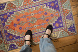 Overhead view of a vintage distressed Oushak rug showing its terracotta and purple colors for scale.