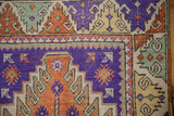 Corner of a distressed Oushak rug with geometric borders in aubergine, terracotta, and seafoam green.