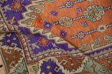 Stylized dragon motifs in aubergine, terracotta, and seafoam on a folded vintage Oushak rug.