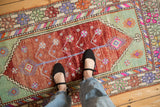 Distressed Oushak rug runner with faded burgundy dye lot variations and colorful borders.