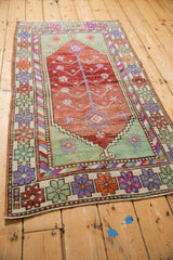 Distressed Oushak rug corner showing floral border, pinwheel motifs, and magenta, mint, tangerine tones.