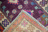 Folded distressed Oushak rug corner reveals heavily abrashed aubergine, ivory fields, geometric motifs.