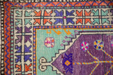 Close-up of the vintage Oushak rug's arrowed and checkered borders in aubergine, mint, and orange.