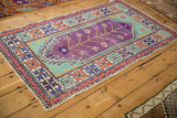 Angled shot of a vintage distressed Oushak rug with bold aubergine, mint, and orange geometric patterns.