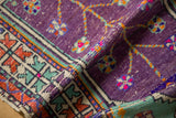 Close-up of a folded Oushak rug's aubergine pile, checkered bands, and arrowed border.
