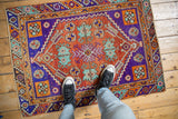 Distressed Oushak rug with pops of rust, violet, and turquoise geometric patterns underfoot.