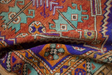 Folded vintage distressed Oushak rug pile featuring serrated patterns in rust, violet, and mint.