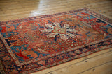Angled view of an antique Farahan Sarouk rug, showcasing its bold medallion, rust field, and deep indigo border.