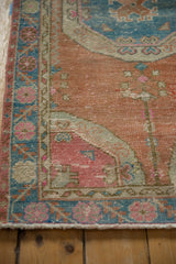 Distressed Oushak rug runner corner, showing pink quarter map spandrel, sky blue border, and fringe.