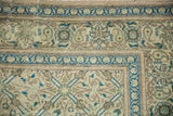 Corner detail of a distressed Turkish carpet with a floral vine border in indigo, beige, and mint green.
