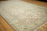 Distressed ivory field with intricate rose blossoms and jade green vines, showing pile wear.