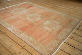 Distressed Oushak rug corner, with abrashed pale cantaloupe field and meandering vine border.