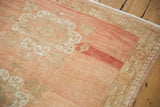 Distressed corner of a vintage Oushak rug, featuring abrashed cantaloupe and ivory vine border.