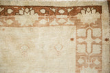 Distressed vintage Oushak rug corner, revealing worn pile and geometric brown motifs on cream.