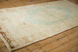 Distressed vintage Oushak carpet, sun-faded cream pile with soft pastel blue and brown hues.