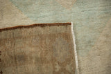 Close-up of distressed Oushak rug corner, showing muted green pile and hand-knotted foundation.