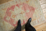 A scale view of a vintage distressed Oushak rug with a faded raspberry red medallion.