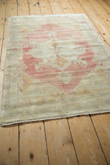 Angled view of the distressed Oushak rug's faded raspberry medallion and time-softened texture.