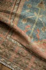 Folded vintage distressed Oushak rug showing textured pile in dusty rose, denim blue, brown.