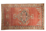 Vintage distressed Kurdish carpet with a faded red field, charcoal medallion, and patterned borders, 6'8