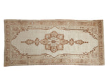 Vintage distressed Oushak runner with a starburst medallion in shades of brown on an open ivory-beige field.