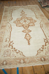 Angled view of the vintage Oushak runner's starburst medallion on an open ivory and beige field.