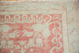 Close-up of the distressed Oushak rug's corner, showing faded raspberry and seafoam green patterns.