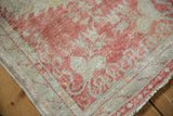 Angled view of the distressed Oushak rug corner showing its mostly even, low-pile wear.