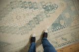 Feet on vintage distressed Oushak rug, faded blue geometric patterns with visible wear.