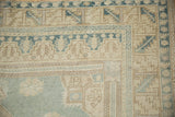 Distressed Oushak rug corner showing worn geometric patterns in pale blue and beige pile.