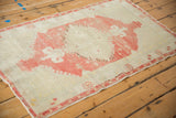 Angled view of a distressed Oushak rug showing its soft, faded raspberry red and ivory design.