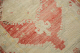 An ivory quatrefoil motif within a pale raspberry red field on a distressed, hand-knotted Oushak rug pile.