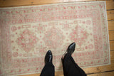 A distressed vintage rug with a soft, faded raspberry and silver pattern shown to scale.