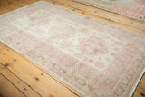 Low-angle view of a distressed Turkish rug with a soft, faded geometric design in raspberry and ivory.