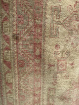 Distressed pile texture featuring faded blush and ivory geometric patterns on the Anatolian rug.
