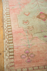 Distressed vintage Oushak rug detail: side selvage, banded border, abrash-rich rose field, primitive blossoms.