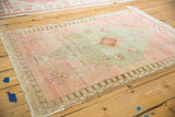 Distressed Oushak rug corner showing dusty rose abrash and primitive blossom motifs.