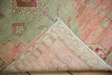Curled corner of a Distressed Oushak rug, showing abrash, sage, rose pile, and hand-knotted back.