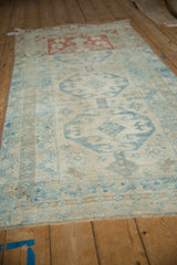 Angled view of a distressed Anatolian rug with blue geometric medallions and a contrasting copper-red end.