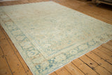 Corner view of a distressed vintage Isparta rug, showing faded green palmette border and soft ivory field.