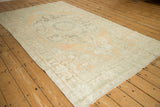 Angled view of a vintage distressed Oushak rug, highlighting its soft seafoam and sandalwood palette.