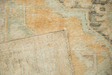 Folded corner of a distressed Oushak carpet showing its hand-knotted foundation and machine-bound edge.