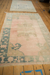 Vintage distressed Oushak rug viewed from an angle, highlighting its pale rose and teal colors.