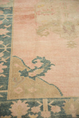 Scrolled serrated leaf motif in dusty teal on the distressed, pale rose ground of a vintage Oushak.