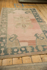 Angled view of a distressed Oushak rug highlighting its abrashed rose field and dusty teal border.