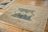 Distressed vintage Isparta rug's corner with faded blue field and soft neutral tones.