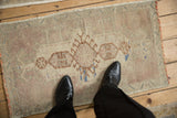 Distressed Oushak rug mat with muted ivory, pale mauve, and brown cartouche design.