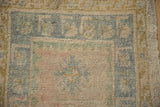 Distressed vintage Oushak rug close-up showing blush, blue-green, and ochre snowflake motif.
